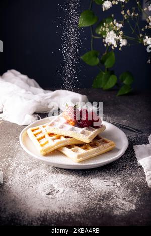 Waffle fatti in casa con fragole, lamponi e zucchero a velo su piatto bianco. Foto Stock