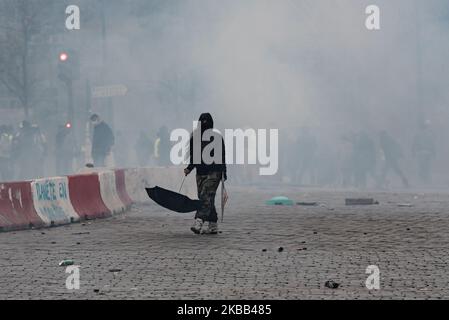 A black masked and hooded demonstrator walks in the middle of tear gas, her hair in the wind, with an umbrella in her hand, this Saturday, November 16, 2019, as the Yellow Vests anniversary demonstration for the movement's first year took place in Paris. A major demonstration was to be held between Place d'Italie and Gare du Nord, but following scenes of violence between the Black Bloc and the police, the prefecture cancelled the march, which gave way to scenes of chaos. (Photo by Samuel Boivin/NurPhoto) Stock Photo