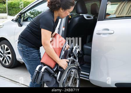 Donna asiatica pieghevole e sollevare la sedia a rotelle nella sua auto. Concetto di accessibilità. Foto Stock