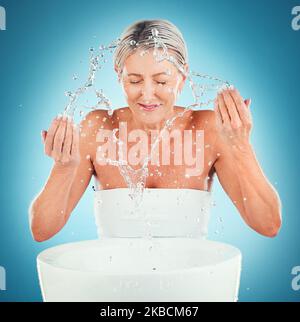 Splash bellezza, senior e cura della pelle per la donna in studio per la cura della pelle, la pelle e l'igiene su sfondo blu mockup. Spruzzi d'acqua, pulizia viso e donna Foto Stock