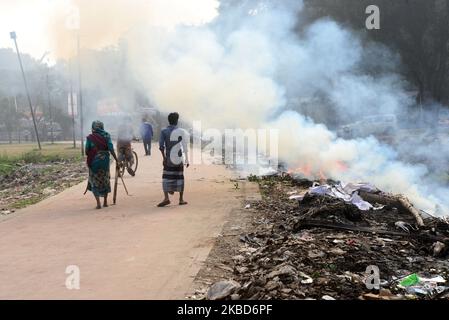 La gente che cammina come la spazzatura sta bruciando accanto ad una strada in un parco a Dhaka, Bangladesh, il 18 dicembre 2019. Il Bangladesh, uno dei paesi più densamente popolati del mondo, ha lottato per lungo tempo contro l’inquinamento atmosferico, mentre Dhaka continua ad essere tra le città più inquinate. Le principali fonti di inquinamento, secondo lo studio, sono i combustibili solidi per uso domestico, le polveri da costruzione, le centrali elettriche a carbone, la produzione di mattoni, i trasporti e le attrezzature diesel, tra gli altri. La qualità dell’aria in Asia è rimasta ostinatamente povera; soprattutto in Bangladesh, dove l’intera popolazione h Foto Stock