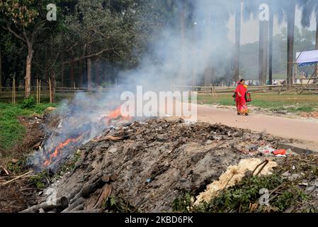 La gente che cammina come la spazzatura sta bruciando accanto ad una strada in un parco a Dhaka, Bangladesh, il 18 dicembre 2019. Il Bangladesh, uno dei paesi più densamente popolati del mondo, ha lottato per lungo tempo contro l’inquinamento atmosferico, mentre Dhaka continua ad essere tra le città più inquinate. Le principali fonti di inquinamento, secondo lo studio, sono i combustibili solidi per uso domestico, le polveri da costruzione, le centrali elettriche a carbone, la produzione di mattoni, i trasporti e le attrezzature diesel, tra gli altri. La qualità dell’aria in Asia è rimasta ostinatamente povera; soprattutto in Bangladesh, dove l’intera popolazione h Foto Stock