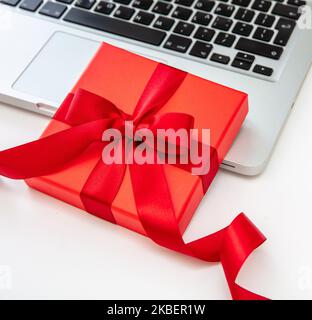 Confezione regalo rossa e computer portatile su sfondo bianco, vista ravvicinata. Natale presenta il modello di shopping in linea Foto Stock