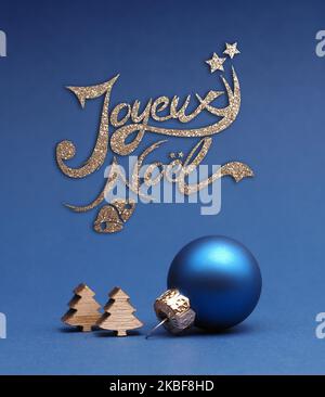 Blu palla albero di Natale con piccole forme albero di legno su uno sfondo di carta blu con testo dorato Joyeux Noel Foto Stock