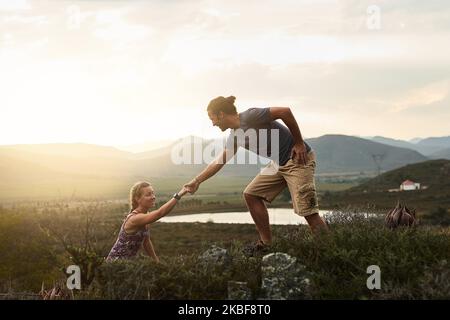 Nature brings out the best in everyone. a friendly young hiker helping his friend climb onto a rock on a mountain trail. Stock Photo