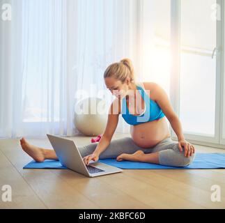 Shes a pregnancy fitness vlogger. a pregnant woman using a laptop during a workout at home. Stock Photo