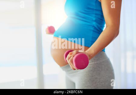 Rimanere forte con la sua gravidanza. Una donna incinta che lavora fuori con i pesi a casa. Foto Stock