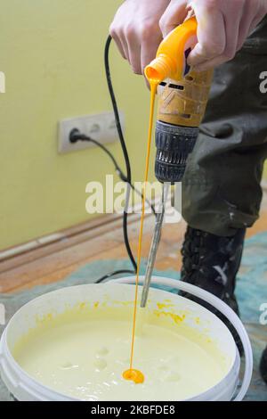 il pittore versa il colorante giallo in un secchio di vernice bianca Foto Stock