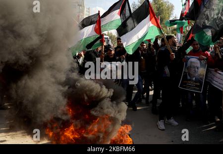 I dimostranti palestinesi cantano slogan e fanno sventolare bandiere palestinesi mentre si trovano a bordo di pneumatici fiammeggianti durante una protesta contro la prevista proposta di piano di pace del presidente degli Stati Uniti Donald Trump a Gaza il 28 gennaio 2020. (Foto di Majdi Fathi/NurPhoto) Foto Stock