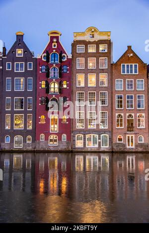 Le famose case da ballo colorate con autentica architettura olandese, fiancheggiano edifici tradizionali con luci. Le case illuminate sull'acqua del bacino del canale di Damrak sono una famosa attrazione turistica, un punto di riferimento vicino alla stazione ferroviaria centrale, un'importante attrazione turistica, ad Amsterdam, Olanda, Paesi Bassi come visto dopo il tramonto, durante la magica ora blu, crepuscolo e notte. Amsterdam, Paesi Bassi (Foto di Nicolas Economou/NurPhoto) Foto Stock