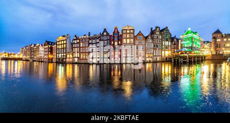 Le famose case da ballo colorate con autentica architettura olandese, fiancheggiano edifici tradizionali con luci. Le case illuminate sull'acqua del bacino del canale di Damrak sono una famosa attrazione turistica, un punto di riferimento vicino alla stazione ferroviaria centrale, un'importante attrazione turistica, ad Amsterdam, Olanda, Paesi Bassi come visto dopo il tramonto, durante la magica ora blu, crepuscolo e notte. Amsterdam, Paesi Bassi (Foto di Nicolas Economou/NurPhoto) Foto Stock
