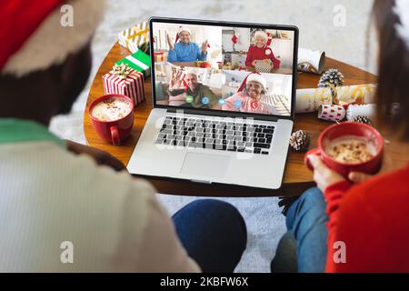 Coppia diversa con decorazioni natalizie che hanno videochiamata con amici diversi felici Foto Stock