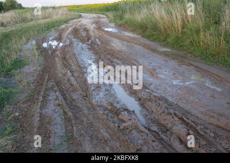 Fango e pozzanghere sulla strada sterrata con colline di sabbia sullo sfondo. Foto Stock