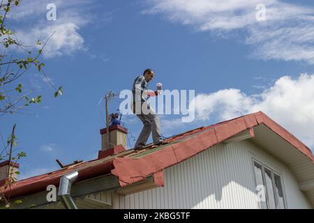 Un uomo sta sul tetto per dipingere un tetto sulla casa Foto Stock