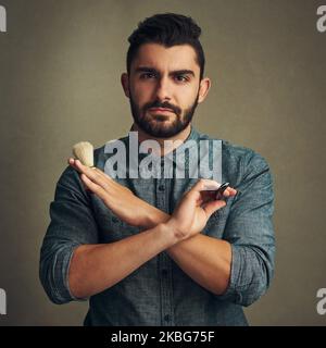 Mantiene la barba in forma. Studio shot di un bel giovane uomo che tiene un rasoio dritto e una spazzola da barba nelle sue mani. Foto Stock