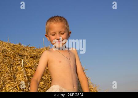 Un ragazzino su un campo vicino ad una paglia chiuse gli occhi al tramonto Foto Stock