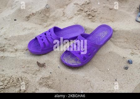 sulla sabbia sono le pantofole viola delle donne Foto Stock