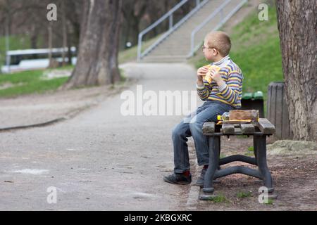 ragazzo che mangia fast food su una panchina del parco Foto Stock