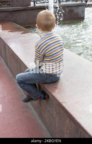 guarda la fontana seduta su una recinzione di pietra sul retro Foto Stock