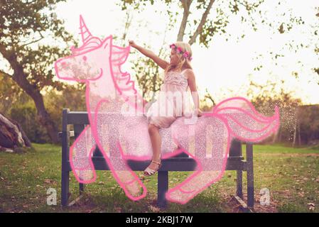 Ogni principessa si sposta al tramonto su un unicorno. Spara una bambina adorabile in sella a un unicorno giocattolo rosa all'aperto. Foto Stock