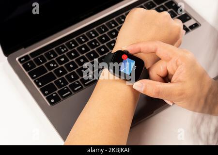 Icona e-mail sullo schermo dello smartwatch, donna che consegna il notebook toccando l'icona e-mail sullo schermo dello smartwatch. Lavoratrice d'ufficio seduto su una scrivania bianca. Foto Stock