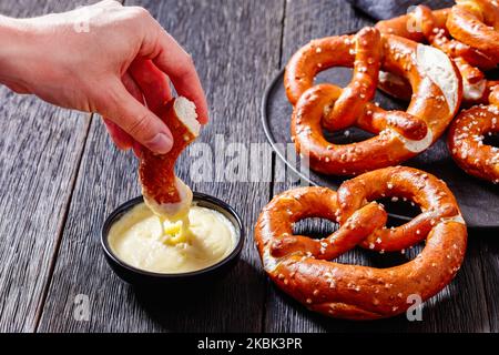 donna immerge un pezzo di morbido pretzel in salsa di formaggio, vista orizzontale dall'alto, primo piano Foto Stock