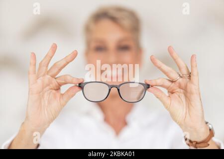 Visione, vista e occhiali nelle mani con sfocatura, la donna ha scarsa vista oculare tenendo gli occhiali in sfondo sfocato. Assistenza sanitaria, assicurazione medica e. Foto Stock