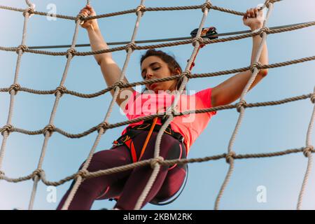 Giovane arrampicatore che ha difficoltà a pendere sulla parete di corde nel parco avventura Foto Stock