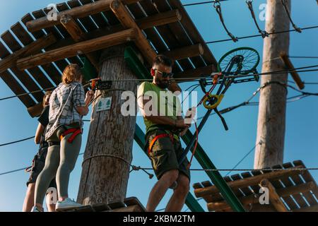 Gruppo di abili scalatori di roccia in attesa di andare sul prossimo ostacolo al traguardo nel parco avventura Foto Stock