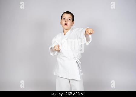 Un ragazzino in kimono pratica il karate, fa pugni con le mani in avanti. Foto Stock