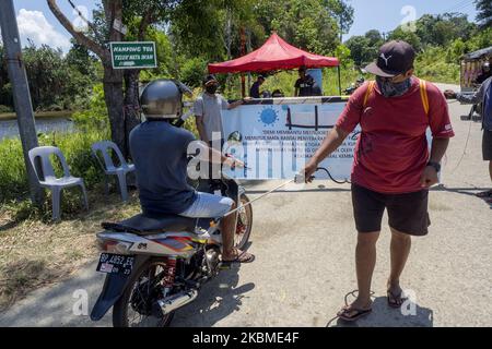 I residenti spruzzano liquido disinfettante e controllano la temperatura corporea sui veicoli utilizzati dai migranti che entreranno nell'area di Kampung Tui, Batam, Isole Riau, 15 aprile 2020. Un certo numero di Kampung tua a Batam ha implementato la quarantena di aree indipendenti come uno sforzo per prevenire e tagliare la diffusione di COVID-19 (Foto di Teguh Prihatna/NurPhoto) Foto Stock