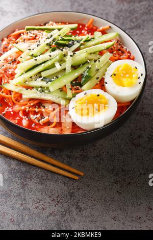 Korean Spicy Noodles Bibim Guksu ontop Boiled Egg Traditional Food Popular dish closeup in the bowl on the table. Vertical Foto Stock