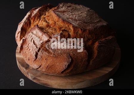 Pane fresco rotondo su un asse di legno con fondo nero Foto Stock