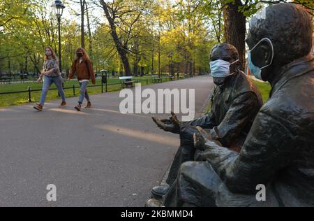 Two young ladies walk by a statue of Stefan Banach and Otton Nikodym with medical masks seen in Krakow's Planty Park, as Poles can now enjoy green space again. From today (April 20), the ban on moving, traveling and staying in public places has been lifted. Public parks, forests and beaches have been reopened, with the exception of playgrounds and sports facilities. Children over 13 years can move without parents. covering mouth and nose in public still remains compulsory. Playgrounds, and sports facilities remain closed. On Monday, April 20, 2020, in Krakow, Poland. (Photo by Artur Widak/NurP Stock Photo