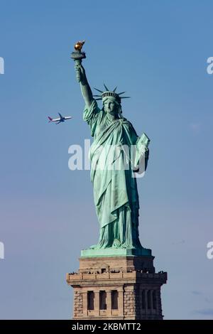 Statua della libertà come si vede durante una giornata senza nuvole cielo blu e un aereo Delta Air Lines che vola dietro. La statua ha turisti e visitatori a Liberty Island Manhattan, New York City, Stati Uniti, da un traghetto in mare. L'iconica statua in rame raggiunge i 93m metri sopra il mare ed è stata dedicata il 28 ottobre 1886. Fu progettata dallo scultore francese Frédéric Auguste Bartholdi e la sua struttura metallica fu costruita da Gustave Eiffel, la scultura fu un dono del popolo francese. Oggi è una popolare attrazione turistica, una destinazione di viaggio, punto di riferimento per NYC e gli Stati Uniti uno dei più reco Foto Stock