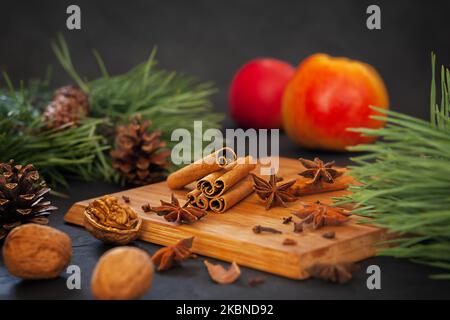 Profumati bastoncini di cannella con anice, mele e noci su un asse di legno su sfondo nero Foto Stock