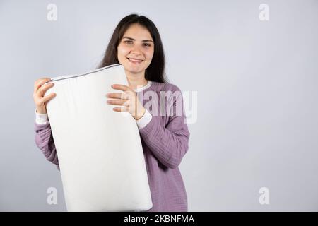 Bella donna brunetta in mussola porpora pigiama pigiami dormiente tiene un cuscino ortopedico, un posto per il testo Foto Stock