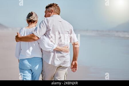Amore, coppia anziana e spiaggia per camminare, vacanza e felice di essere amorevole insieme, viaggio o abbraccio. Romanticismo, uomo maturo e donna anziana abbracciano Foto Stock