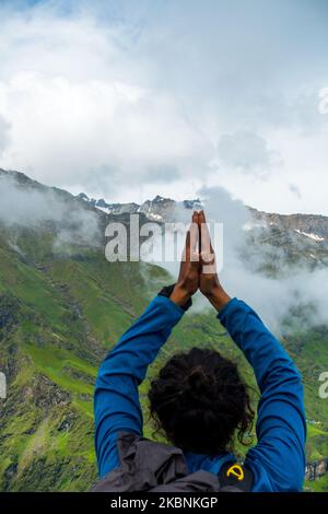 Luglio 14th 2022, Himachal Pradesh India. Un uomo che tiene una posa in testa Namaste con le mani piegate verso Shrikhand Mahadev Peak, lo Shivling, un symbo Foto Stock