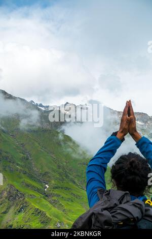 Luglio 14th 2022, Himachal Pradesh India. Un uomo che tiene una posa in testa Namaste con le mani piegate verso Shrikhand Mahadev Peak, lo Shivling, un symbo Foto Stock