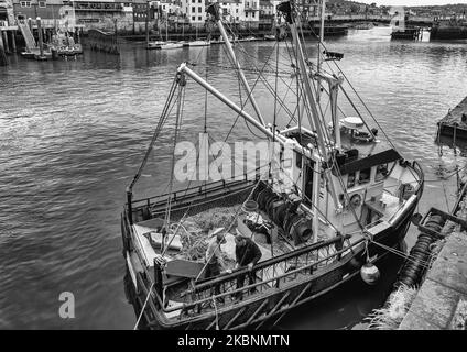 La poppa di un peschereccio con reti a strascico sul ponte. Due pescatori assistono ad un problema con una catena. Il porto è oltre. Foto Stock