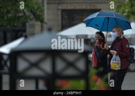 Due giovani donne che indossano maschere protettive camminano nella piazza principale del mercato di Cracovia durante il tempo piovoso. La pioggia è tornata nella zona di Cracovia e il tempo variabile con temperature comprese tra 15 e 20 gradi C è previsto per i prossimi 10 giorni. Lunedì 25 maggio 2020 a Cracovia, Polonia. (Foto di Artur Widak/NurPhoto) Foto Stock