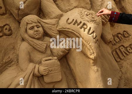 Lo scultore della sabbia palestinese Rana Ramlawi conclude una nuova opera d'arte in commemorazione della Giornata Mondiale del Rifugiato, una giornata dedicata dall'Assemblea Generale delle Nazioni Unite per sensibilizzare la popolazione alla situazione dei rifugiati in tutto il mondo, a Gaza il 20 giugno 2020, Raffigurante una donna che trasporta un bambino e un sacco di farina recante il logo dell'Agenzia delle Nazioni Unite per il soccorso e l'occupazione dei profughi palestinesi (UNRWA) con un bambino dietro che tiene una tanica d'acqua, il tutto davanti a una mappa del mondo. – Più di 1,5 milioni di persone vivono in 58 campi profughi palestinesi riconosciuti in Giordania, Leban Foto Stock