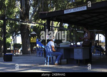 Un cassiere in una maschera protettiva serve i clienti in una caffetteria nel parco. Limassol, Cipro, Martedì, Giugno 23, 2020 il Ministero della Salute di Cipro dal Giugno 24 abroga la regola che limita le riunioni ad un massimo di 10 persone. Così, dal giugno 24, il numero massimo consentito di partecipanti alle riunioni in sale chiuse è di 75 persone, per sale aperte - 150 persone. Questa regola si applica alle cerimonie nuziali, ai battesimi, ai concerti, alle feste, alle riunioni private nelle case (in questo caso, i proprietari della casa sono considerati anche partecipanti) e a tutte le altre forme di riunioni di massa. Più grande e più numerou Foto Stock