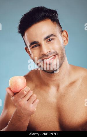 Apple, fitness e uomo in uno studio ritratto prima di mangiare frutta sana su una dieta vegana e stile di vita benessere. Nutrizione, sfondo blu e felice Foto Stock