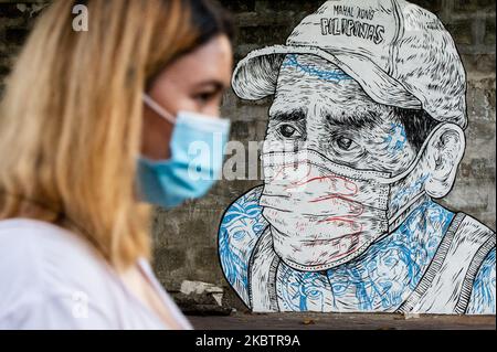 Una donna passa davanti a un murale raffigurante un uomo la cui bocca e il naso sono coperti con una maschera e una mano a Quezon City, Filippine il 17 luglio 2020. Il numero totale di casi confermati nelle Filippine è salito a 63, 001 dopo che oggi sono stati registrati 1.841 nuovi casi (Foto di Lisa Marie David/NurPhoto). Foto Stock