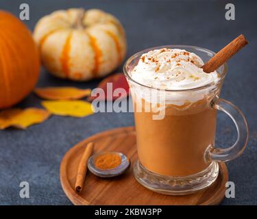 Latte di spezie di zucca con panna montata in una tazza di vetro in un piatto di legno Foto Stock