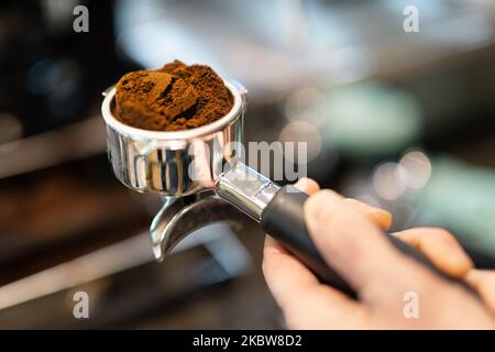 Una mano che tiene un portafiltro con caffè appena macinato accatastato all'interno in un'atmosfera dal vivo. Foto Stock