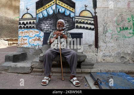 Un uomo palestinese si siede di fronte a un murale della sacra Kaaba, a Gaza City, 27 luglio 2020.la stagione hajj 2020, che è stata ridotta drammaticamente per includere solo circa 1.000 pellegrini musulmani come l'Arabia Saudita batte un aumento di coronavirus, è destinato a iniziare il 29 luglio. Circa 2,5 milioni di persone provenienti da tutto il mondo di solito partecipano al rituale che si svolge in diversi giorni, incentrato sulla città Santa della Mecca. L'hajj di quest'anno si terrà in base a rigorosi protocolli igienici, con accesso limitato ai pellegrini sotto i 65 anni e senza alcuna malattia cronica. (Foto di Majdi Fathi Foto Stock