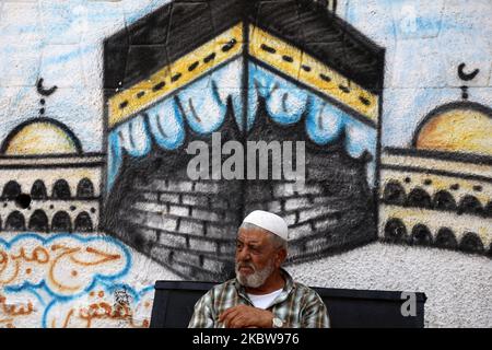 Un uomo palestinese si siede di fronte a un murale della sacra Kaaba, a Gaza City, 27 luglio 2020.la stagione hajj 2020, che è stata ridotta drammaticamente per includere solo circa 1.000 pellegrini musulmani come l'Arabia Saudita batte un aumento di coronavirus, è destinato a iniziare il 29 luglio. Circa 2,5 milioni di persone provenienti da tutto il mondo di solito partecipano al rituale che si svolge in diversi giorni, incentrato sulla città Santa della Mecca. L'hajj di quest'anno si terrà in base a rigorosi protocolli igienici, con accesso limitato ai pellegrini sotto i 65 anni e senza alcuna malattia cronica. (Foto di Majdi Fathi Foto Stock